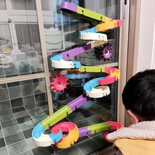 Colorful toy track with gears on a glass door, child playing.