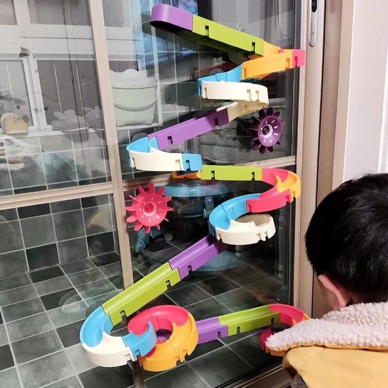 Colorful toy track with gears on a glass door, child playing.