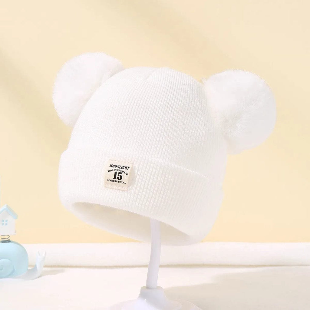 White knit beanie with pom-poms on a stand against a light yellow background