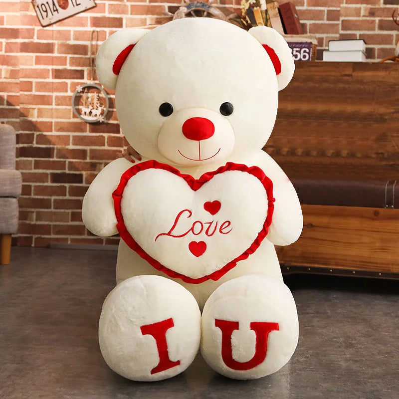 White teddy bear with a red heart and 'I Love U' message on a wooden floor.