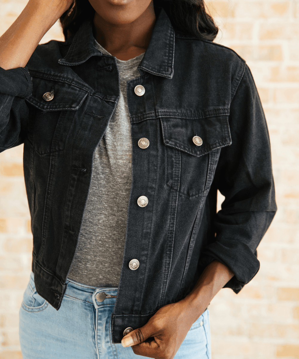 Person wearing a black denim jacket over a gray shirt.