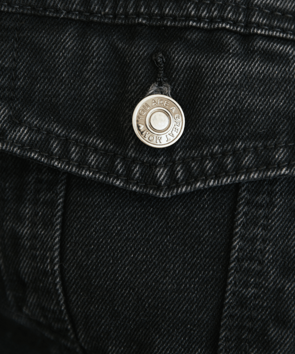 Close-up of a black denim jacket with a button and brand logo.
