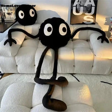 Black plush ball pillow with large eyes tucked into a couch corner for cozy seating.