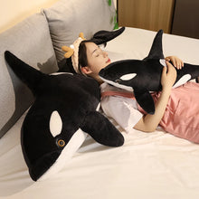 Black and white orca whale plush doll used as a body pillow on a bed for sleeping, lounging, and cosy bedroom decorating.