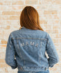 Person wearing a denim jacket with 'MAMA' on the back against a brick wall.