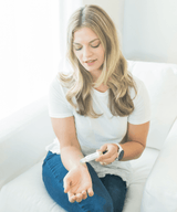 Woman sitting on a white couch using an essential oil roller.