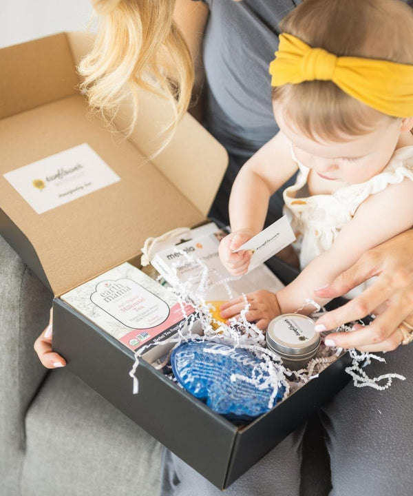 Person opening a box with baby items, including a blue soap bar and a yellow headband.