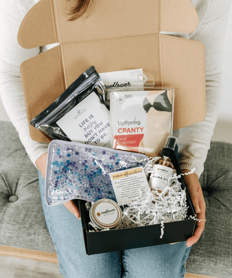 Person holding a box of assorted items including a book and small containers.