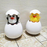 Two cartoon penguin and duck toys in eggshells on a tiled floor.