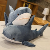 Large plush shark toy on a bed with a wooden shelf and lamp in the background