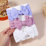 Three colorful bow hair accessories on a white box with a hand holding it.
