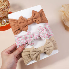 Three decorative bows, two brown and one floral, held by a hand on a white surface.