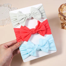 Three colorful hair bows on a white tray held by a hand against a beige background.