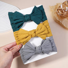 Three colorful bow hair accessories on a white surface with a hand holding one of them.