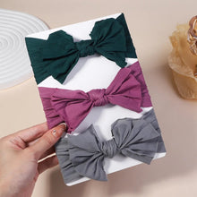 Three fabric bows in green, purple, and gray on a white box with a hand holding the box.