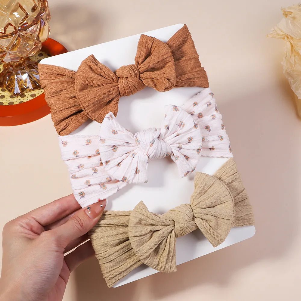 Three fabric bows in different colors held by a hand on a light background