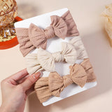 Three fabric hair bows in different colors on a white tray with a hand holding one of them.