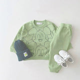 Green Mickey Mouse-themed sweatshirt, pants, blue beanie, and white sneakers.