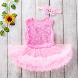 Pink baby dress with floral lace and matching headband on a wooden surface with decorative elements.