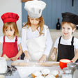 Three children in chef hats and aprons at a kitchen counter with baking ingredients