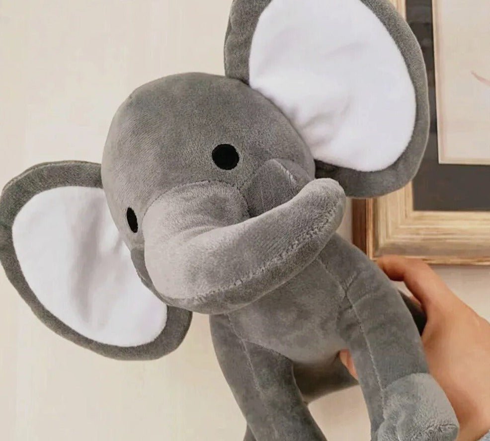 Gray plush elephant toy held by a hand against a neutral background