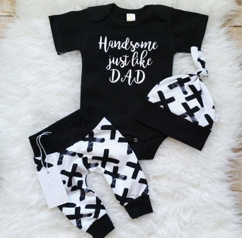 Black and white baby outfit with 'Handsome just like DAD' text on a fluffy white surface.