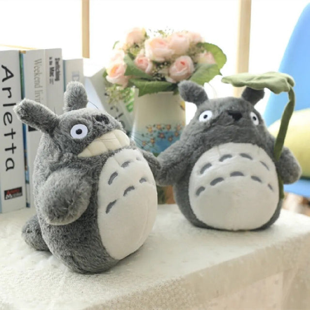 Two plush toys resembling a famous animated character on a surface with books and flowers in the background.