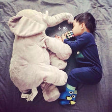 Child lying beside an elephant plush pillow toy on the bed for bedtime comfort and play.