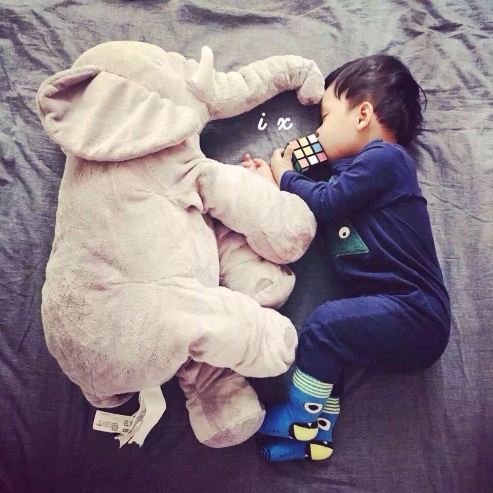Child lying beside an elephant plush pillow toy on the bed for bedtime comfort and play.