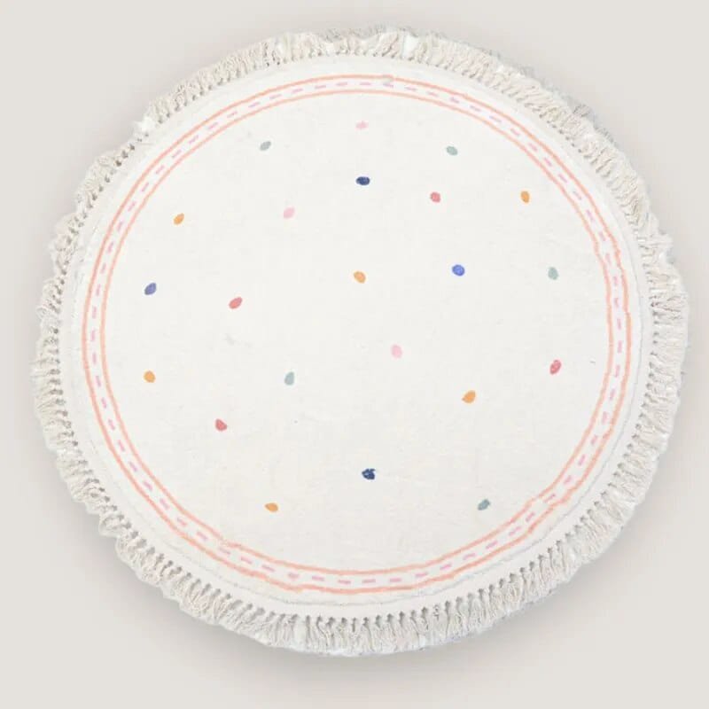 Round white placemat with colorful dots and fringed edge.