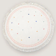 Round white placemat with colorful dots and fringed edge.