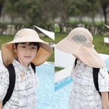 Child wearing a large beige sun hat by a poolside with trees in the background