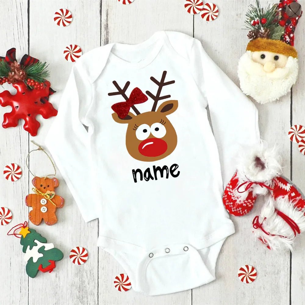 White baby onesie with reindeer design and 'name' text, surrounded by Christmas decorations on a wooden surface. (option 4)