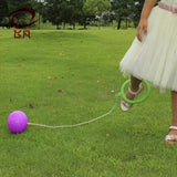Person in a white dress with a green hoop and purple ball on grass