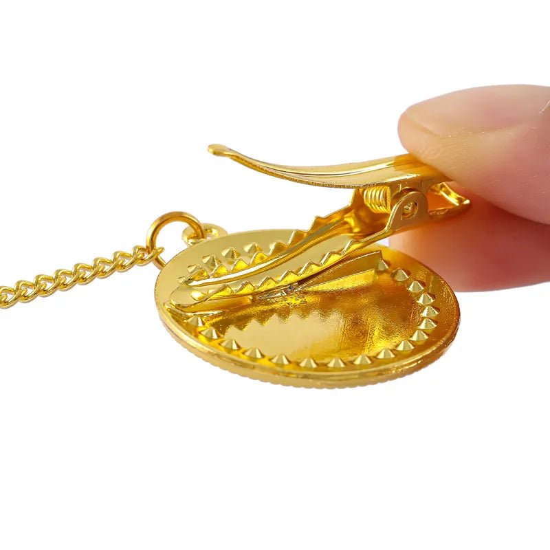 Gold clip-shaped pecifier holder on a chain held by a hand against a white background
