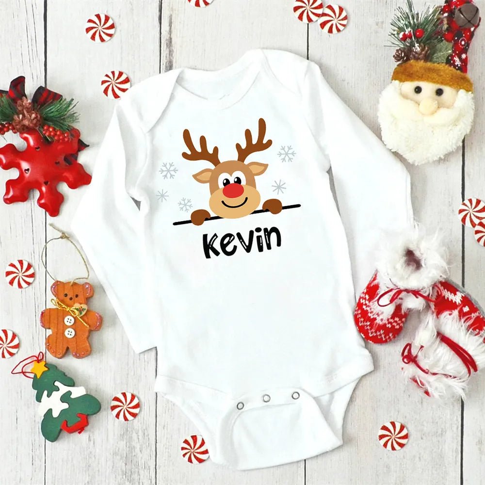 White baby onesie with a reindeer design and 'Kevin' text, surrounded by Christmas decorations on a wooden surface.