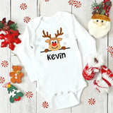 White baby onesie with a reindeer design and 'Kevin' text, surrounded by Christmas decorations on a wooden surface.