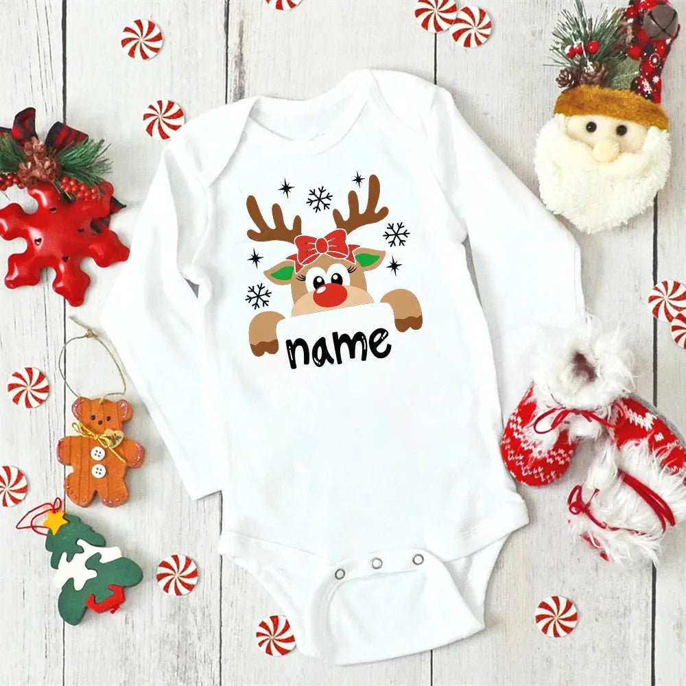 White baby onesie with reindeer design and 'name' text on a wooden surface with Christmas decorations. (option 4)