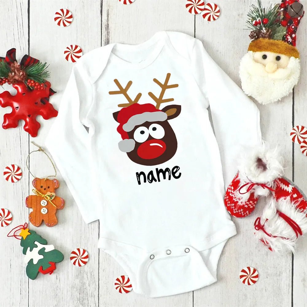 White baby onesie with reindeer design and 'name' text, surrounded by Christmas decorations on a wooden surface. (option 21)