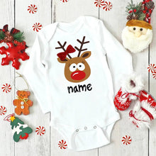White baby onesie with reindeer design and 'name' text, surrounded by Christmas decorations on a wooden surface. (option 12)