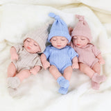 Three baby dolls wearing knitted hats and outfits on a soft white surface