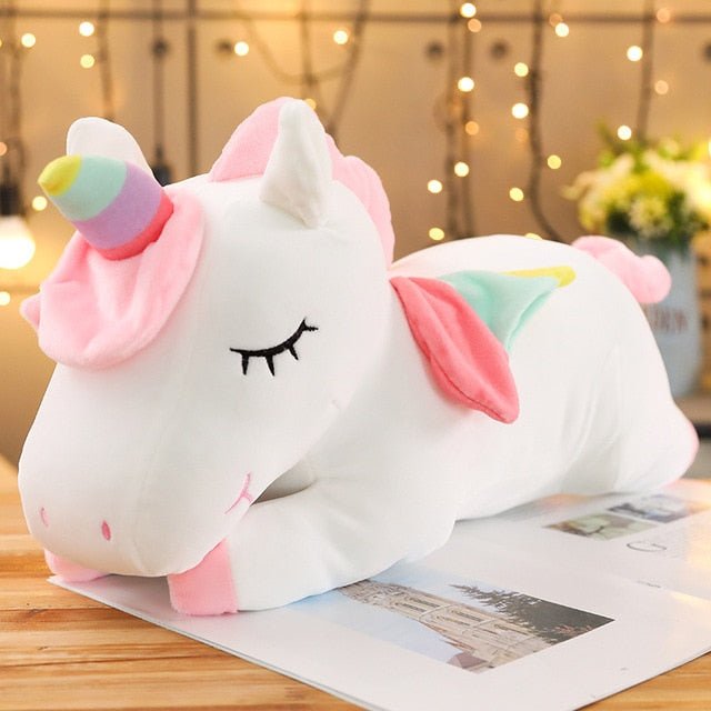 Plush unicorn toy with a colorful horn on a wooden surface.