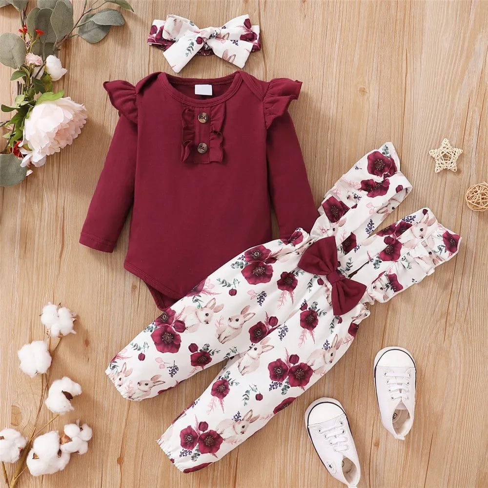 Baby outfit with maroon top, floral pants, and white sneakers on a wooden surface.