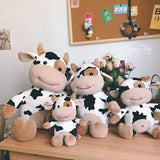Four cow-themed plush toys on a wooden surface with a bulletin board in the background.