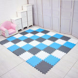 Checkered foam puzzle mat in blue, gray, and white on a wooden floor with a pink chair and white cabinet in the background.