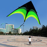 Person flying a large green and black kite in an open square with buildings in the background