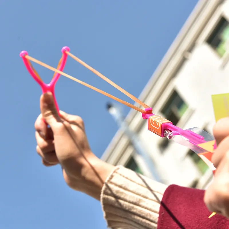 Person holding a pink and orange slingshot against a clear blue sky.