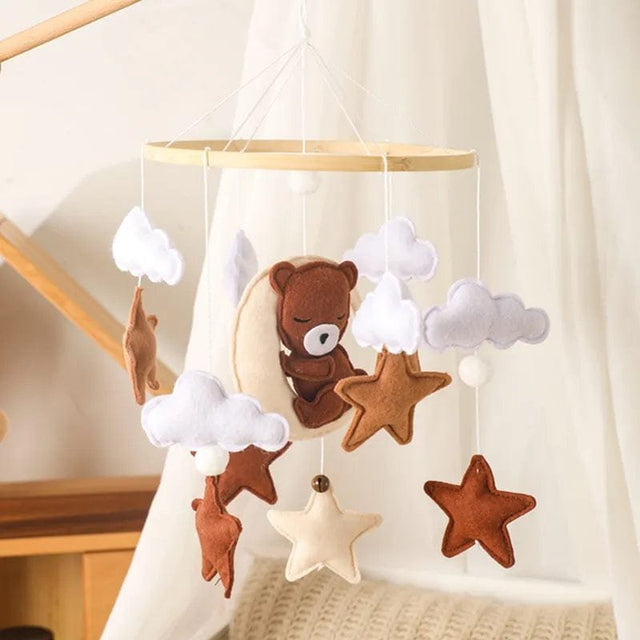 Baby mobile with teddy bear and star decorations hanging against a neutral background