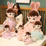Woman with a collection of plush toys resembling children with bunny ears on a bed.