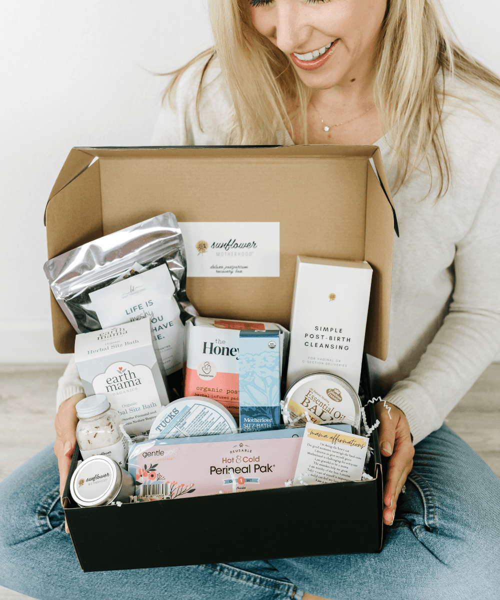 Woman holding a box filled with various items including skincare products and a book titled 'Sunflower'.